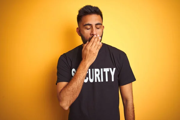 Arab indian hispanic safeguard man wearing security uniform over isolated yellow background bored yawning tired covering mouth with hand. Restless and sleepiness.