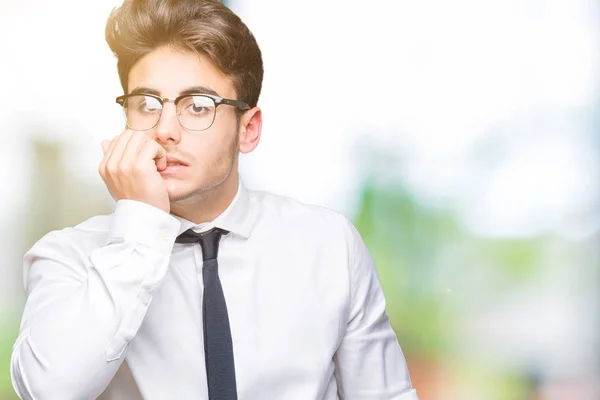 Young business man wearing glasses over isolated background looking stressed and nervous with hands on mouth biting nails. Anxiety problem.