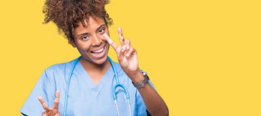 Genç Afro-Amerikan doktor kadın parmaklarını zafer işareti yaparken gösterilen kamera seyir gülümseyen izole arka plan yüzünden. İki numaralı.