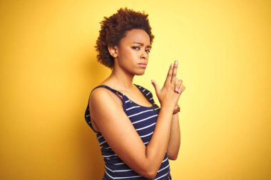 Beauitul afro-amerikan kadın izole sarı arka plan üzerinde yaz t-shirt giyen el hareketi ile sembolik silah holding, çekim silah öldürme oynarken, kızgın yüz