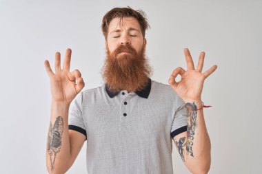 Genç kızıl İrlandalı adam izole beyaz arka plan üzerinde duran gri polo giyen dinlenmek ve gözleri parmakları ile meditasyon jest yapıyor kapalı gülümseyerek. Yoga konsepti.