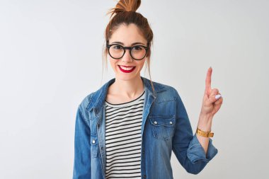 Redhead kadın çizgili t-shirt denim gömlek ve gözlük izole beyaz arka plan üzerinde gösteren ve emin ve mutlu gülümserken parmak sayısı bir ile işaret giyiyor.
