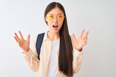 Genç Çinli öğrenci kadın gözlük ve sırt çantası giyen izole beyaz arka plan üzerinde deli ve deli bağırarak ve agresif ifade ve kollar kaldırdı ile bağırıyor. Hayal kırıklığı kavramı.