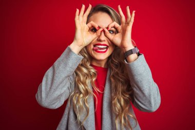 Genç güzel iş kadını kırmızı izole arka plan üzerinde duran zarif ceket giyen dürbün dil dışarı yapışmasını gibi ok jest yapıyor, gözleri parmaklardan bakarak. Çılgın ifade.