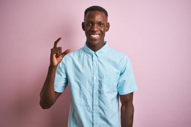 Izole pembe arka plan üzerinde duran mavi rahat gömlek giyen Afrikalı Amerikalı adam gülümseyerek ve emin parmakları görünümlü ve kamera ile küçük boyutlu işareti yapıyor ile gesturing. Ölçü kavramı.