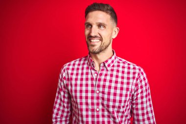 Kırmızı izole arka plan üzerinde genç yakışıklı adam yüzünde gülümseme, doğal ifade ile yan bakıyor. Gülmekten emin.