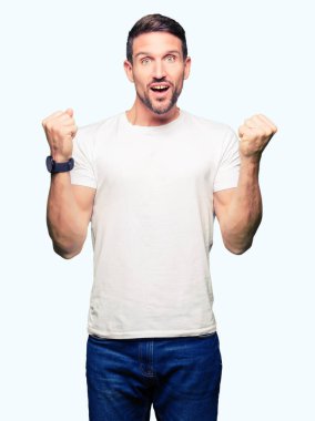 Casual beyaz kutluyor t-shirt giyen yakışıklı adam şaşırttı ve başarı için kaldırdı kollarını açarak hayret ve gözleri açık. Kazanan kavramı.