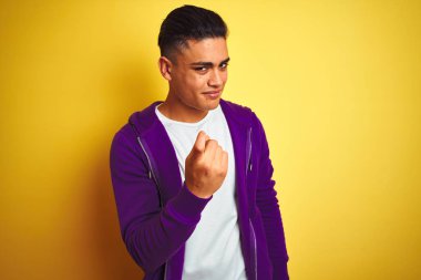 İzole sarı arka plan Beckoning üzerinde duran mor sweatshirt giyen genç Brezilyalı adam mutlu ve gülümseyen davet eden el ile buraya jest geliyor