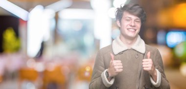 Yakışıklı delikanlı izole arka plan başarı işareti el ile pozitif jest yapıyor üzerinde kış palto giyiyor başparmak gülümseyen ve mutlu. Neşeli bir ifadeyle, kazanan jest kameraya bakıyor.