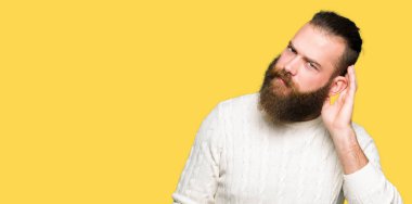 Bir işitme söylenti ya da dedikodu için dinleme kulak üzerinde el ile gülümseyen kış kazak giyen genç hipster adam. Sağırlık kavramı.