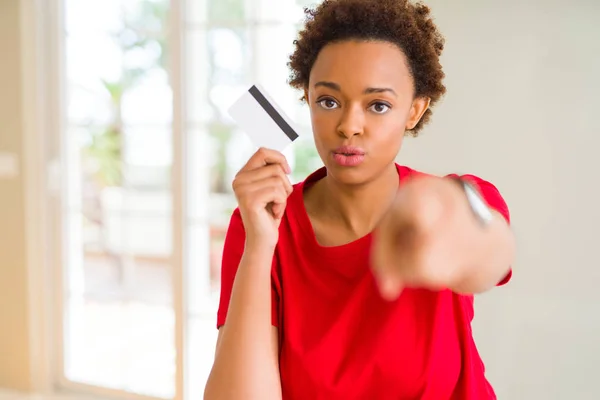 Young african american woman holding credit card pointing with finger to the camera and to you, hand sign, positive and confident gesture from the front