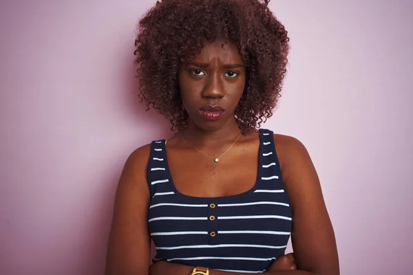 孤立したピンクの背景に懐疑的で神経質なストライプのTシャツを着た若いアフリカのアフロ女性は 十字架の腕で顔に失望した表情をしています 否定的な人 — ストック写真
