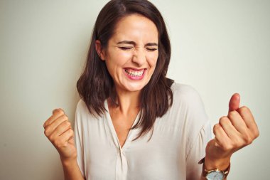 Genç güzel kadın beyaz izole arka plan üzerinde duran rahat gömlek giyen çok mutlu ve heyecanlı kolları kaldırdı ile kazanan jest yapıyor, gülümseyerek ve başarı için çığlık. Kutlama konsepti.