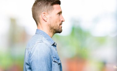Mavi gözlü ve sakal giyen denim ceket yan arayan yakışıklı adam, güvenli bir gülümseme ile doğal yüz ile profil poz rahatlayın.