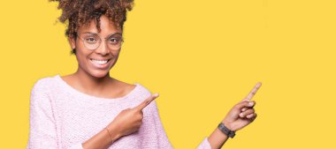 Güzel genç Afro-Amerikan kadın gülümseyerek ve iki elleri ve parmakları ile tarafına işaret kamera bakarak izole arka plan üzerinde gözlük.