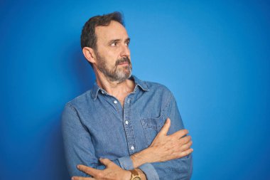 Izole mavi arka plan üzerinde gri saçlı Yakışıklı orta yaş yaşlı adam kolları ile yan bakarak ikna ve kendinden emin geçti