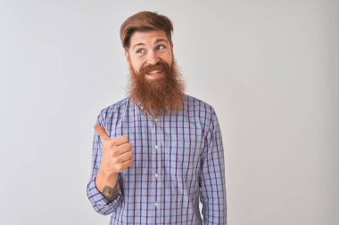Genç kızıl İrlandalı adam izole beyaz arka plan üzerinde duran rahat gömlek giyen mutlu yüz görünümlü gülümseyerek ve başparmak ile yan işaret.
