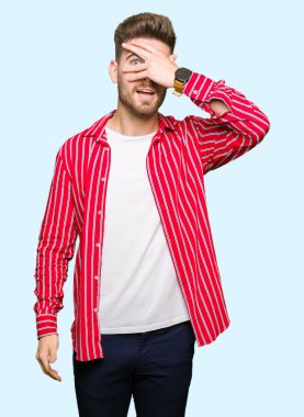 Mahcup ifadeyle parmaklarımın arasından seyir yüz ve gözler el ile kapsayan şok kırmızı gömlek bakmak giyen genç yakışıklı adam.