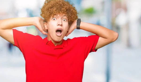 Young handsome man with afro hair wearing red t-shirt Crazy and scared with hands on head, afraid and surprised of shock with open mouth