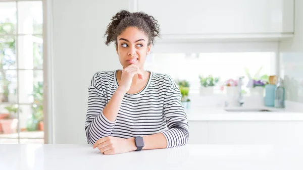 Beautiful african american woman with afro hair wearing casual striped sweater Thinking worried about a question, concerned and nervous with hand on chin