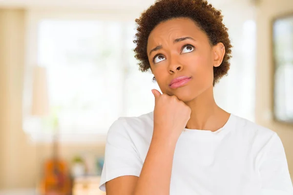 Young beautiful african american woman wearing casual white t-shirt with hand on chin thinking about question, pensive expression. Smiling with thoughtful face. Doubt concept.