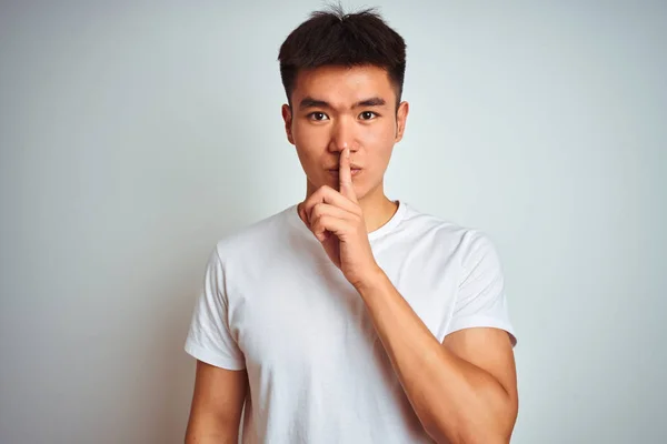 孤立した白い背景の上に立つTシャツを着たアジアの若い中国人男性は 唇に指で静かにするように頼みます 沈黙と秘密の概念 — ストック写真