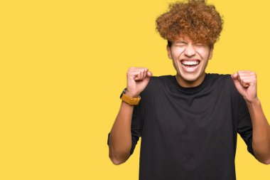 Silah ile başarı için t-shirt heyecanlı siyah giymeyi afro saçlı yakışıklı delikanlı zafer kutluyor gülümseyen kaldırdı. Kazanan kavramı.