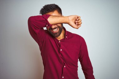 Kırmızı zarif gömlek giyen genç hintli adam kol neşeli ve komik gülümseyerek gözleri kaplayan izole gri arka plan üzerinde duran. Kör kavramı.