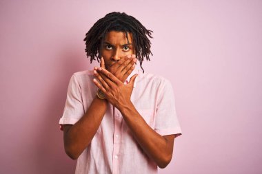 Afro amerikan adam dreadlocks zarif gömlek izole pembe arka plan üzerinde duran giyen hata için elleri ile ağız kapsayan şok. Gizli kavram.