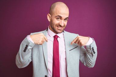 Mor izole arka plan üzerinde takım elbise ve kravat giyen genç iş adamı yüzünde gülümseme ile emin görünümlü, parmakları gururlu ve mutlu kendini işaret.