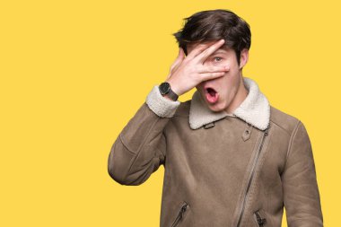 Mahcup ifadeyle parmaklarımın arasından seyir yüz ve gözler el ile kapsayan şok bakmak izole arka plan üzerinde kış ceket giyen genç yakışıklı adam.
