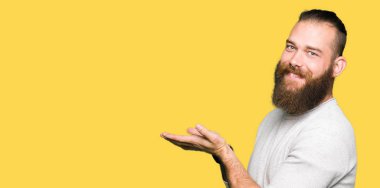 Casual kazak giyen genç sarışın adam el ve reklam mutlu ve kendinden emin gülümseyen sunulması avuç, yanında işaret