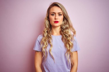 Pembe izole arka plan üzerinde duran mor t-shirt giyen genç güzel kadın yüzünde ciddi ifade ile rahat. Kameraya basit ve doğal bir bakış.