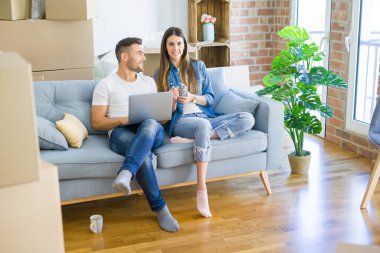 Genç çift yeni bir ev bilgisayar laptop kullanarak kanepede oturan rahatlatıcı, yeni daireye taşımak için mutlu gülümseyen hareket