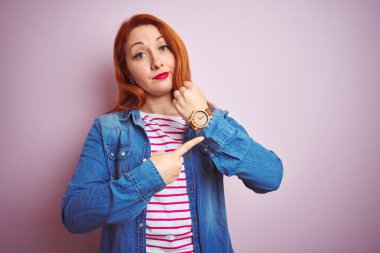 Denim gömlek giyen güzel kızıl saçlı kadın ve izole pembe arka plan üzerinde çizgili t-shirt Acele zaman izlemek için işaret, sabırsızlık, rahat ifade ile kameraya bakarak