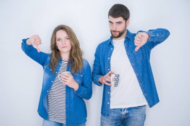 Genç güzel çift kızgın yüz ile beyaz izole arka plan üzerinde bir fincan kahve içme, aşağı başparmak ile sevmediğim gösteren negatif işareti, ret kavramı