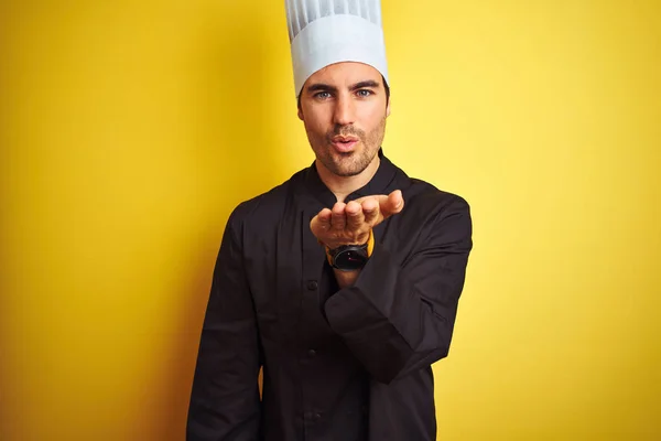 年轻的厨师男子穿着制服和帽子站在孤立的黄色背景 看着相机吹一个吻与手在空中可爱和性感 爱表达 — 图库照片