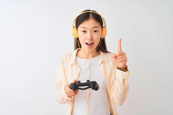 中国玩家妇女玩视频游戏使用耳机在孤立的白色背景惊讶与想法或问题指向手指与快乐的脸 — 图库照片