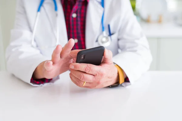 Primo piano delle mani dell'uomo medico utilizzando smartphone e indossando stetho — Foto Stock