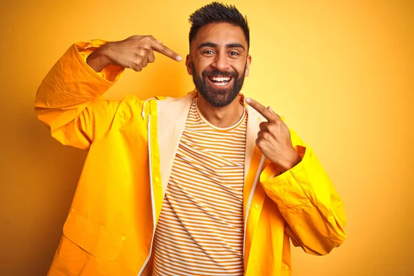 年轻的印度男子穿着雨衣站在孤立的黄色背景上 面带微笑 用手指和嘴指着 牙齿健康概念 — 图库照片