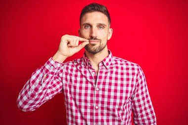 Kırmızı izole arka plan ağız ve dudaklar üzerinde Genç yakışıklı adam parmakları ile zip olarak kapattı. Gizli ve sessiz, tabu konuşma