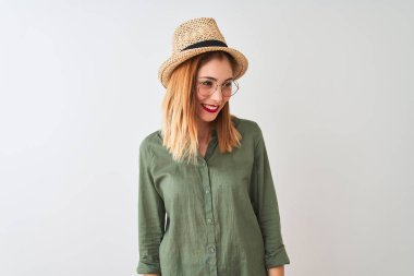 Kırmızı saçlı kadın yeşil gömlek gözlük ve şapka izole beyaz arka plan üzerinde yüz, doğal ifade gülümseme ile yan bakıyor giyiyor. Gülmekten emin.