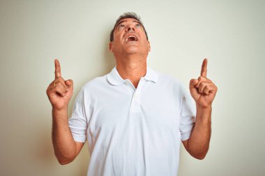 Izole beyaz arka plan üzerinde duran polo giyen Yakışıklı orta yaş adam şaşırttı ve yukarı bakarak ve parmakları ile işaret ve kolları kaldırdı şaşırttı.