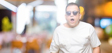 Orta Çağ Arap adam beyaz t-shirt ve güneş gözlüğü izole arka plan üzerinde wearig korkuyor ve sürpriz ifade, korku ve heyecanlı yüz ile şok.