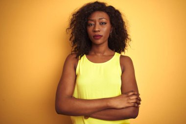 Genç afro-amerikan kadın izole sarı arka plan üzerinde duran t-shirt giyen şüpheci ve sinirli, çapraz kolları ile yüzünde onaylamayan ifade. Negatif kişi.