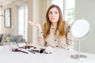 Güzel genç kadın kullanarak kozmetik habersiz ve karışık ifade kolve elleri kaldırdı makyaj. Şüphe kavramı.