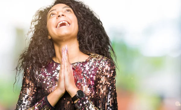 Young beautiful girl with curly hair wearing night party dress begging and praying with hands together with hope expression on face very emotional and worried. Asking for forgiveness. Religion concept.