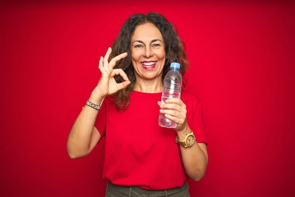 Seniorin Mittleren Alters Hält Plastikwasserflasche Über Rotem Isoliertem Hintergrund Und — Stockfoto