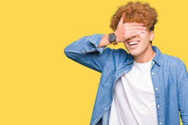 Yakışıklı genç afro saçlı kot ceket gülümseyen ve gözler için sürpriz kapsayan yüz el ile gülüyor. Kör kavramı.