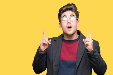 Genç yakışıklı zarif adam hayret ve yukarıya bakıyor ve parmakları ile işaret ve silah kaldırdı sürpriz izole arka plan üzerinde gözlük.